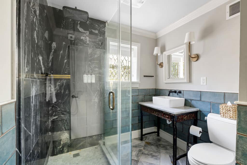 Contemporary bathroom with a glass-enclosed shower, dark marble walls, blue-green tile wainscoting, and a white vessel sink on a dark vanity.