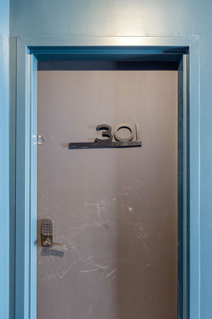 Blue-framed metal door with the number 301 mounted on a horizontal bar and a keypad lock on the left side.