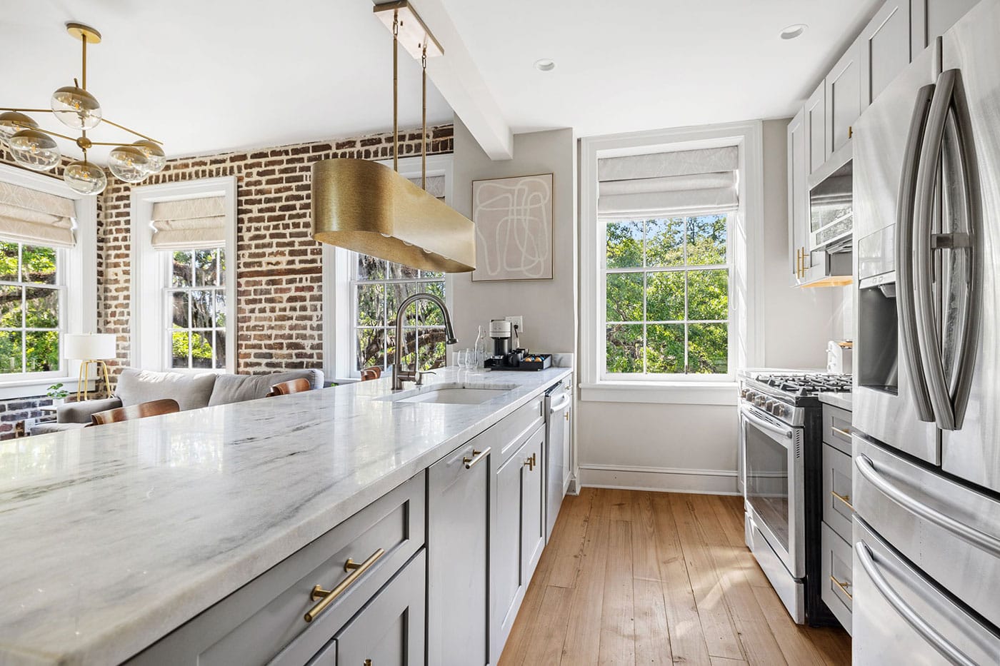 Bright, modern kitchen with marble island, brick accent wall, and stainless steel appliances overlooking a green backyard garden.