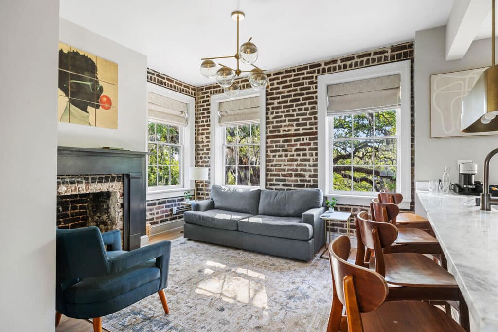 Bright living area with a grey sofa, blue armchair, and three large windows letting in natural light.