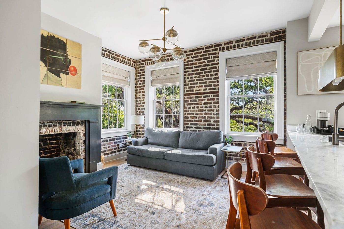 Bright living area with a grey sofa, blue armchair, and three large windows letting in natural light.