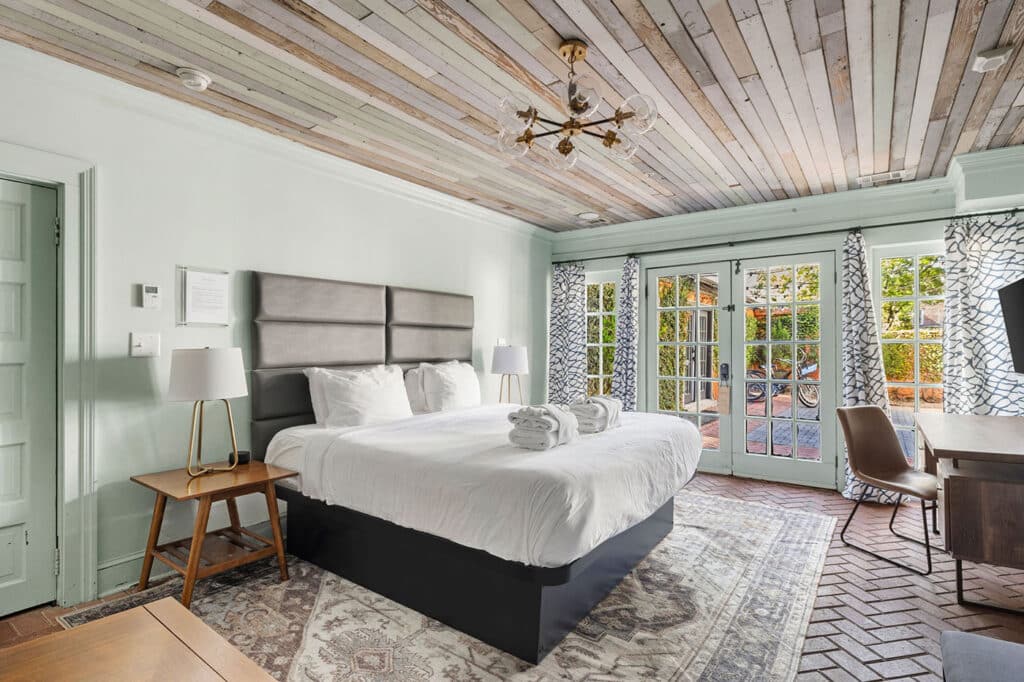 King-size bed with gray headboard, white linens, and matching nightstands in a bright hotel room with lamps on each side.