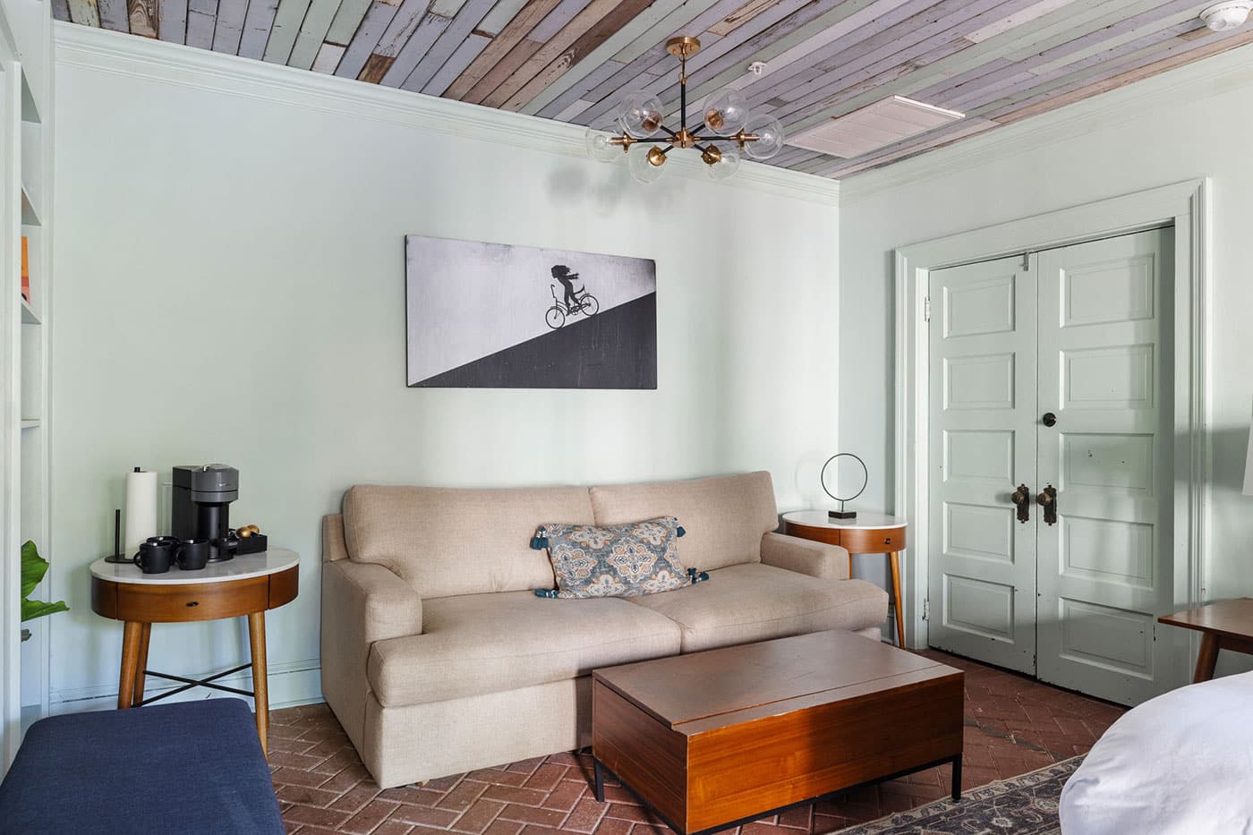 Cozy living room with beige sofa, wooden coffee table, and matching side tables; wall art of a cyclist on a diagonal split background.