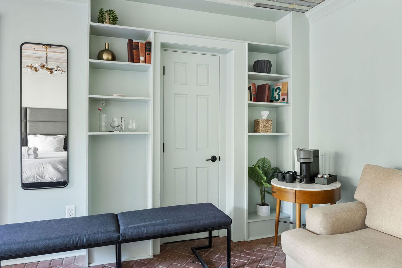 Living area with mint-green built-in shelves around a white door, a blue bench in front, and a round-table coffee setup beside a beige sofa.