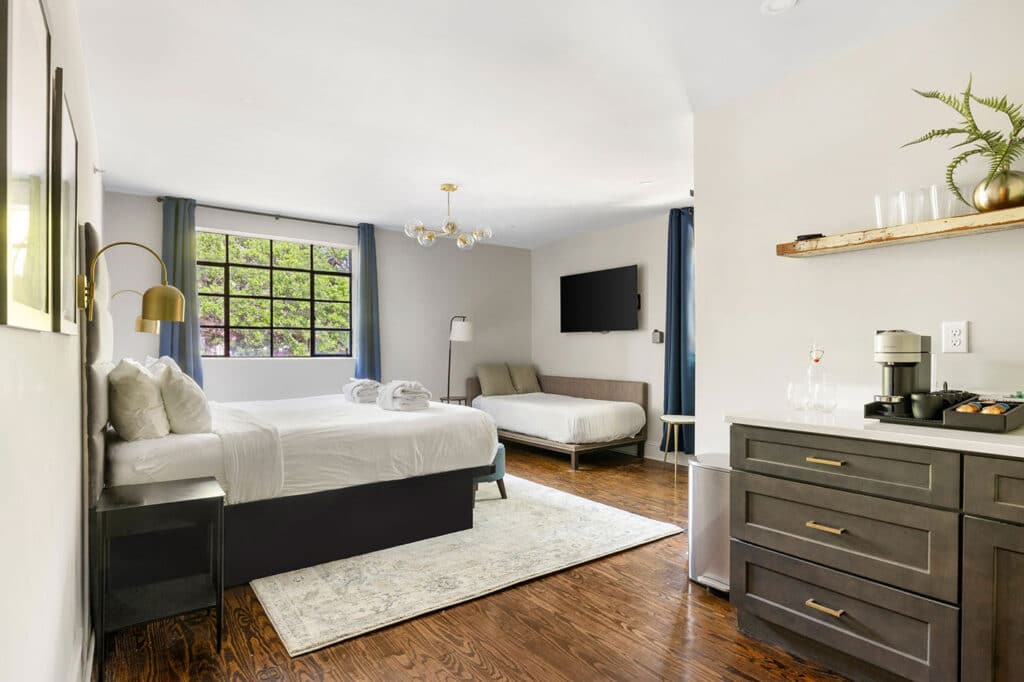 Spacious hotel room with a large bed, a second bed, hardwood floor, and a coffee station on the right.