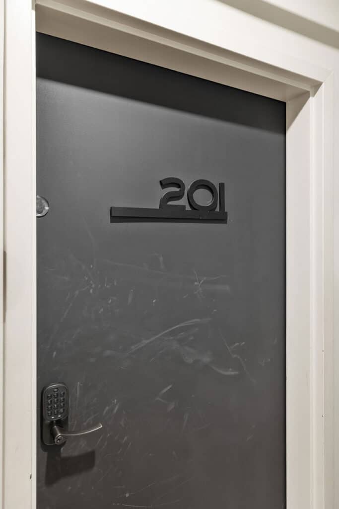 Dark gray apartment door with the number 291 and a keypad lock on the left, white trim around the frame, visible scratches on the door surface