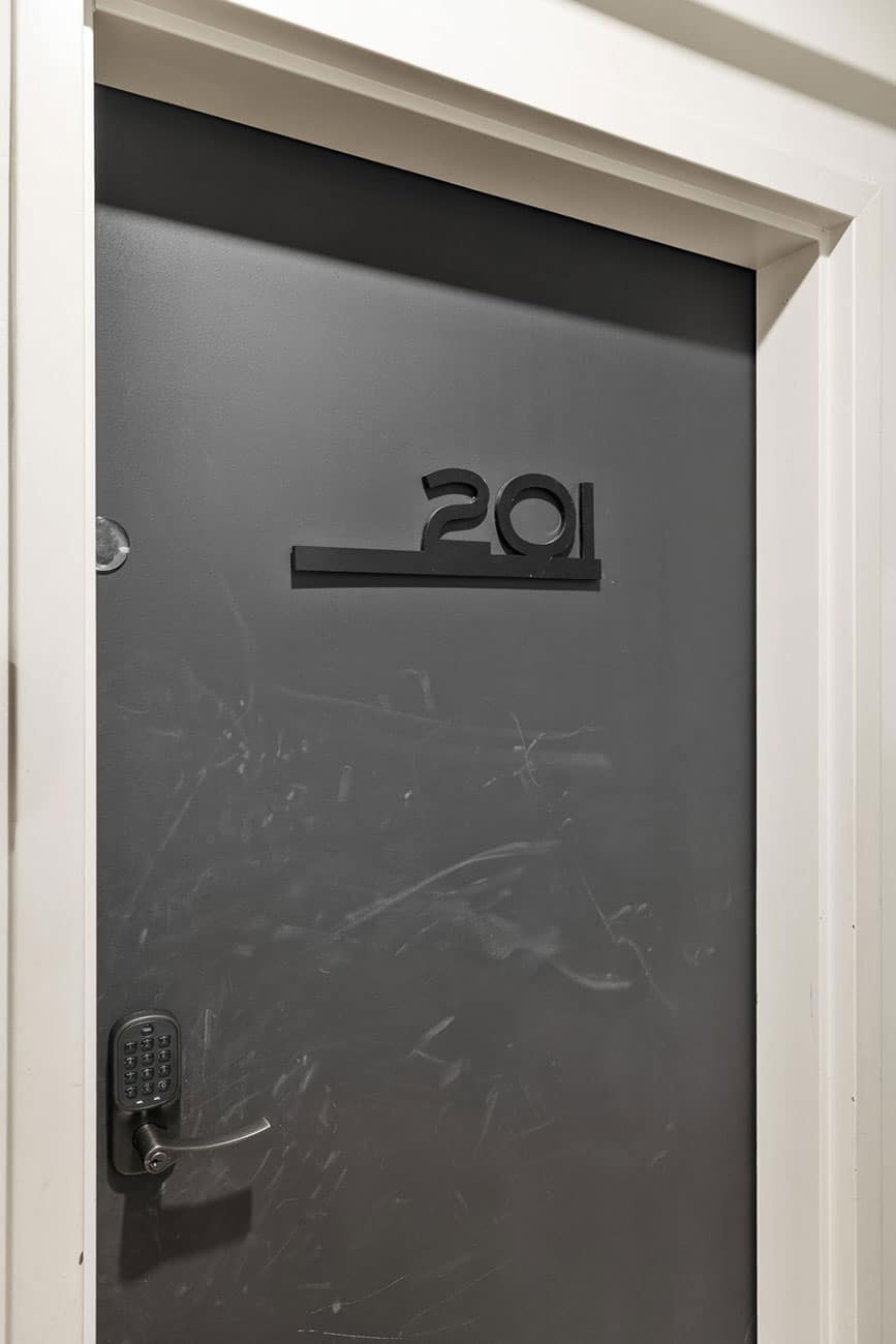 Dark gray apartment door with the number 291 and a keypad lock on the left, white trim around the frame, visible scratches on the door surface
