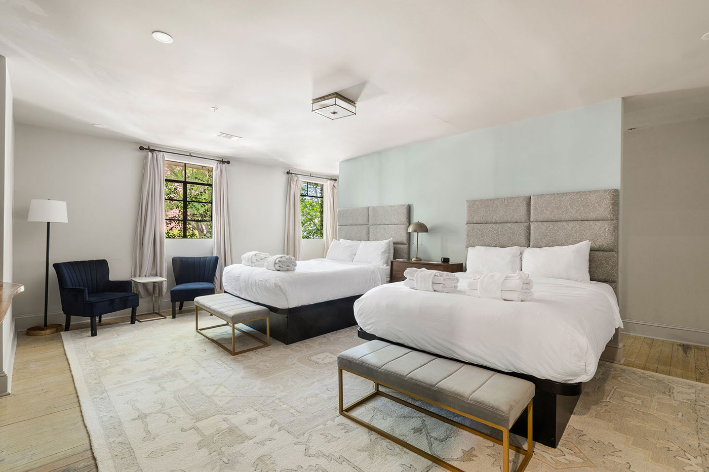 Hotel room with two queen beds, white bedding, a light blue accent wall, and a bench at each foot of the beds.