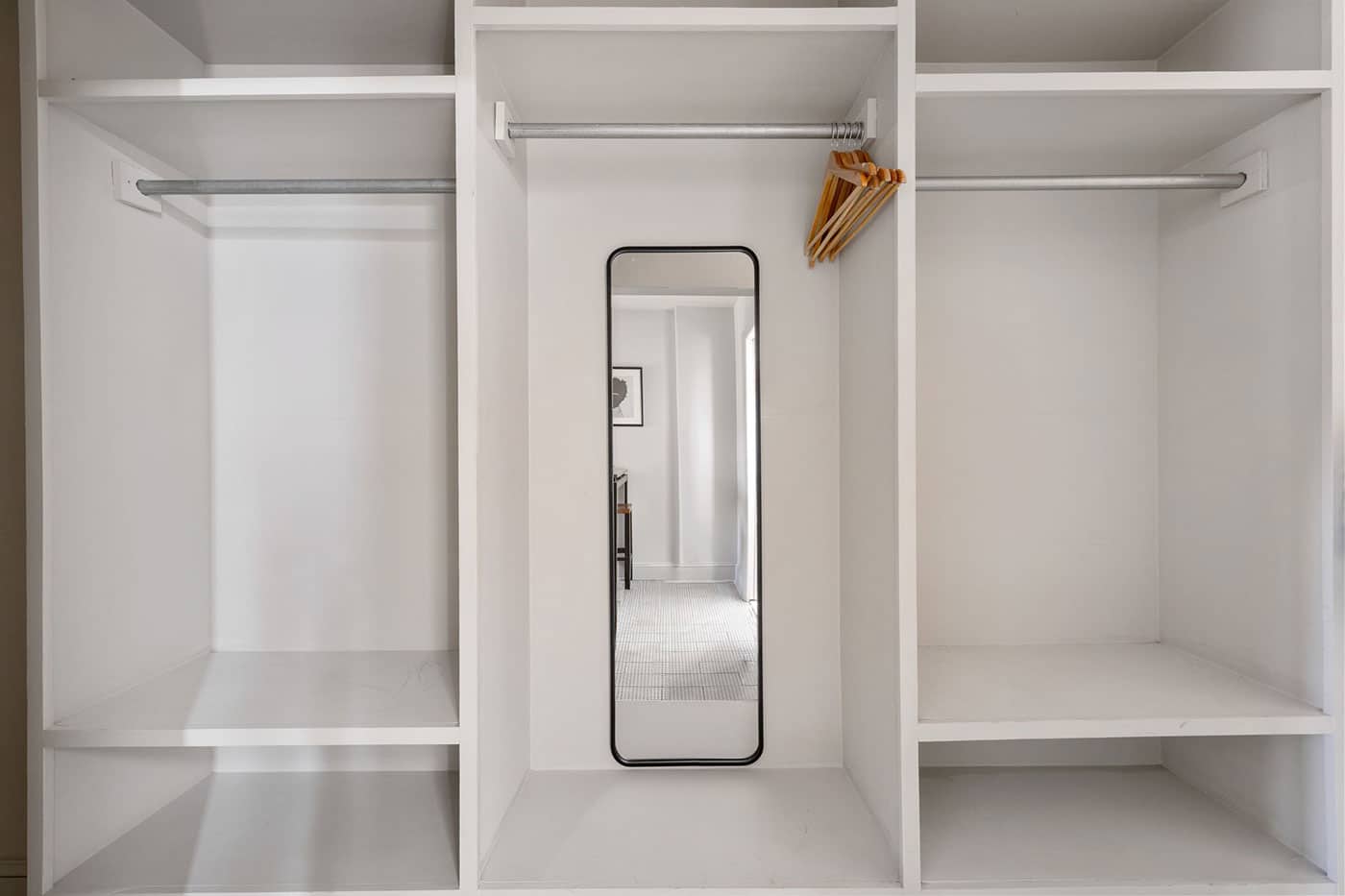 Walk-in closet with white built-in shelves, a central full-length mirror, and a few wooden hangers on the right rod.