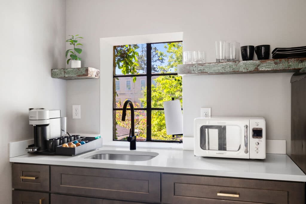 Modern kitchen with a white countertop, dark cabinets, window above sink, coffee maker on the left and microwave on the right.