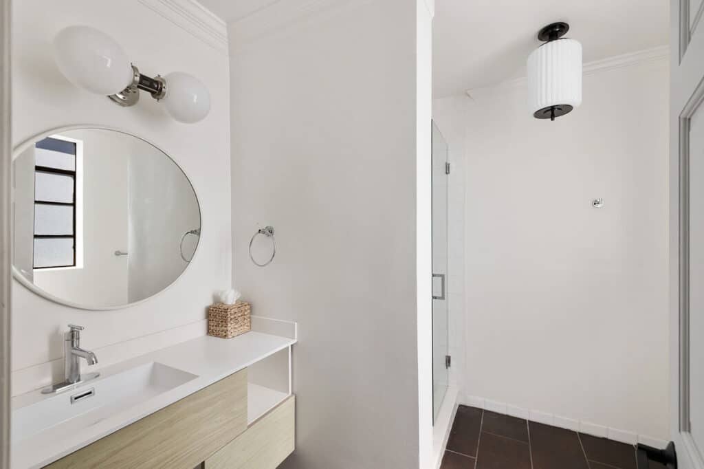 Modern white bathroom with a round mirror above a white countertop and light wood vanity, a tissue box, and chrome faucet.