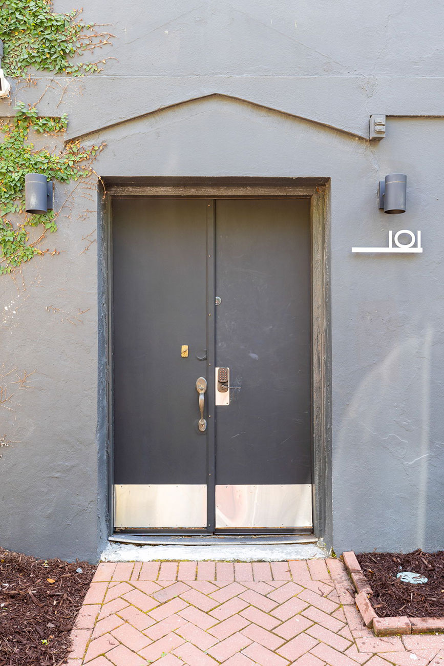 Double metal door set in a gray wall with ivy on the left and a small '101' sign on the right side.