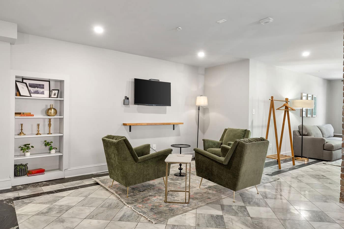 Cozy living area with two olive-green armchairs facing a wall-mounted TV, a small coffee table, and a shelf with decorative items.