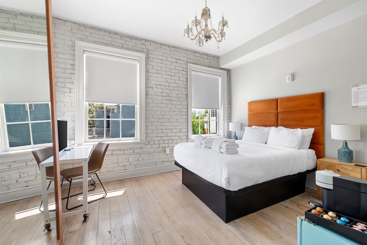 Bright bedroom with white brick walls, a king bed with an orange upholstered headboard, and a crystal chandelier overhead.