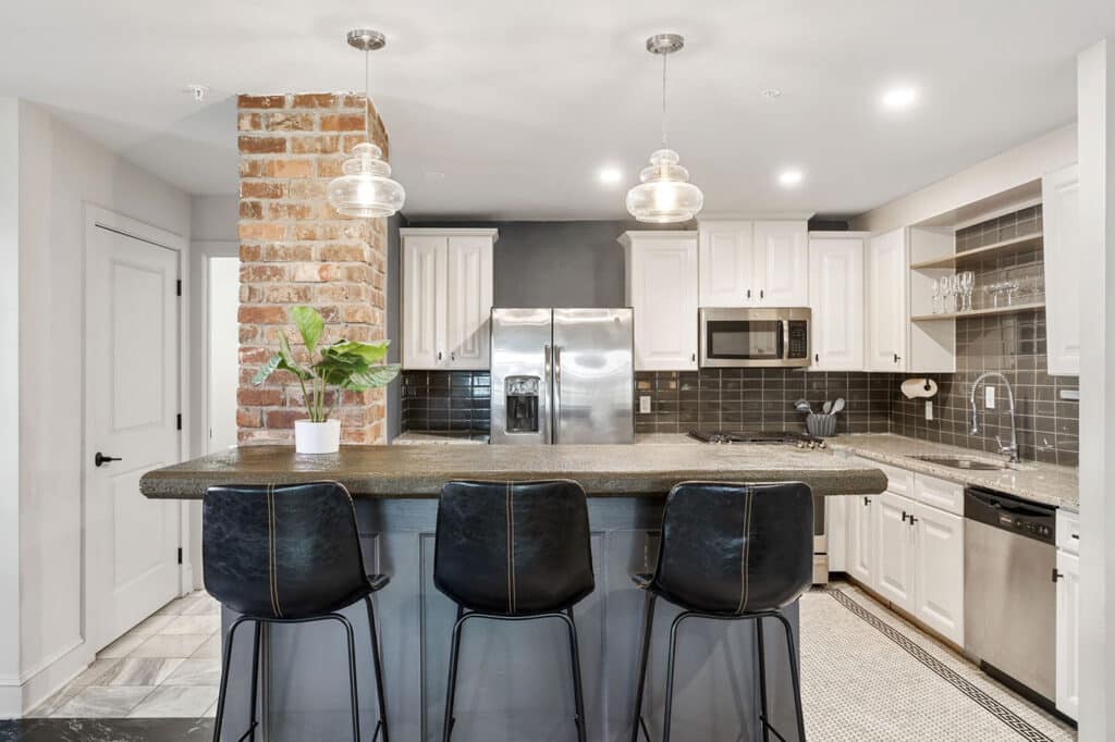 Modern kitchen with brick pillar, island seating for three, white cabinets, stainless steel appliances, and pendant lights.