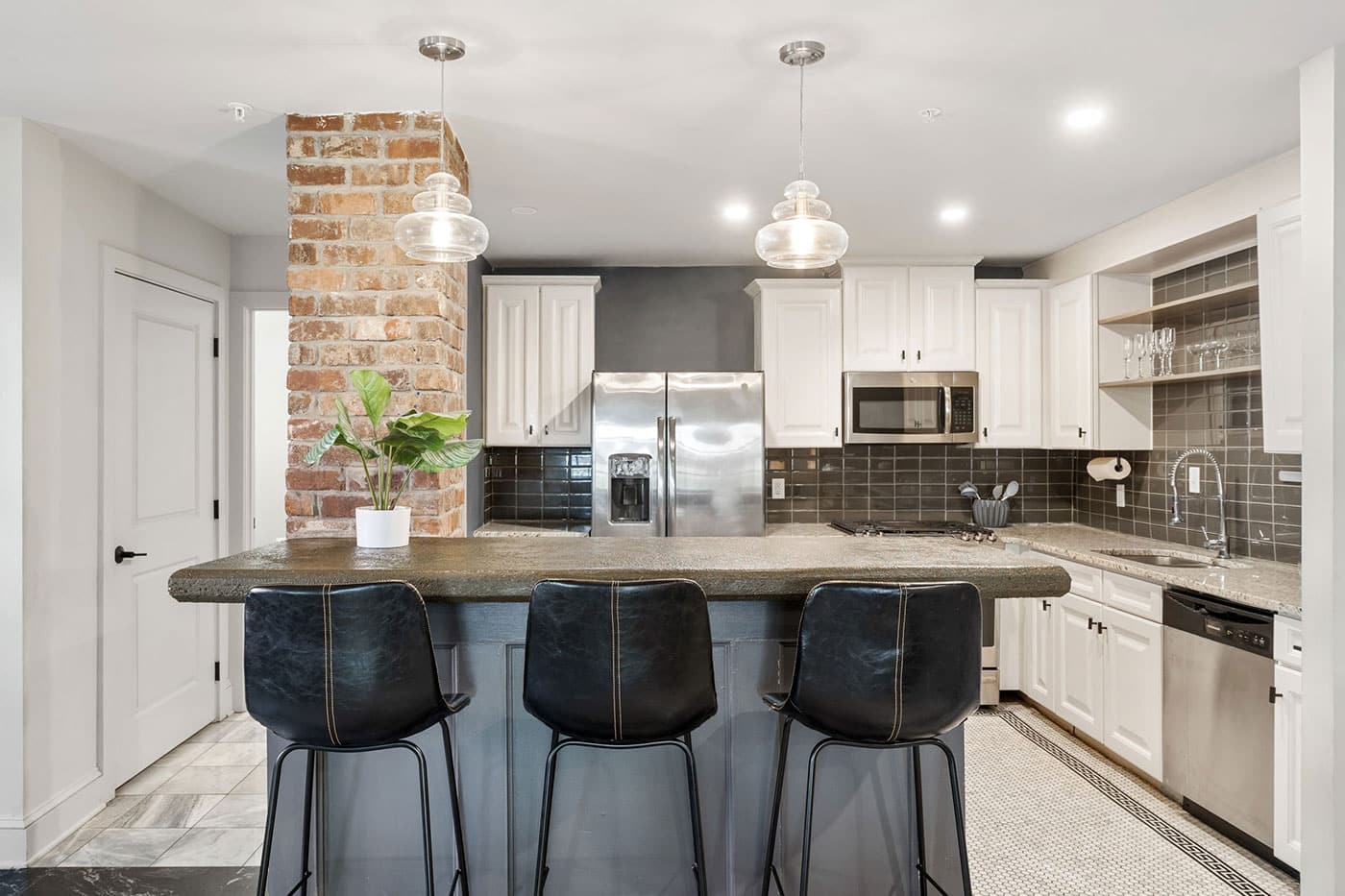 Modern kitchen with brick pillar, island seating for three, white cabinets, stainless steel appliances, and pendant lights.