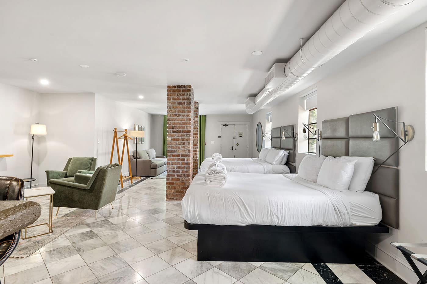 Spacious hotel suite with two queen beds, padded headboards, and a seating area with green chairs.