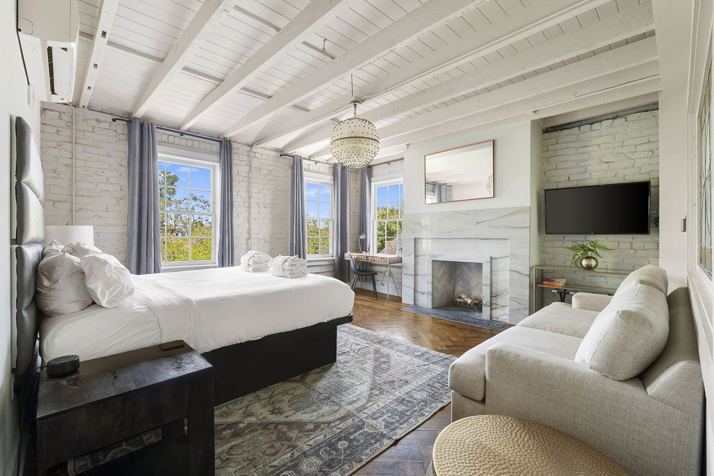 Bright modern bedroom with white brick walls, exposed white beams, a king bed, and a marble fireplace.