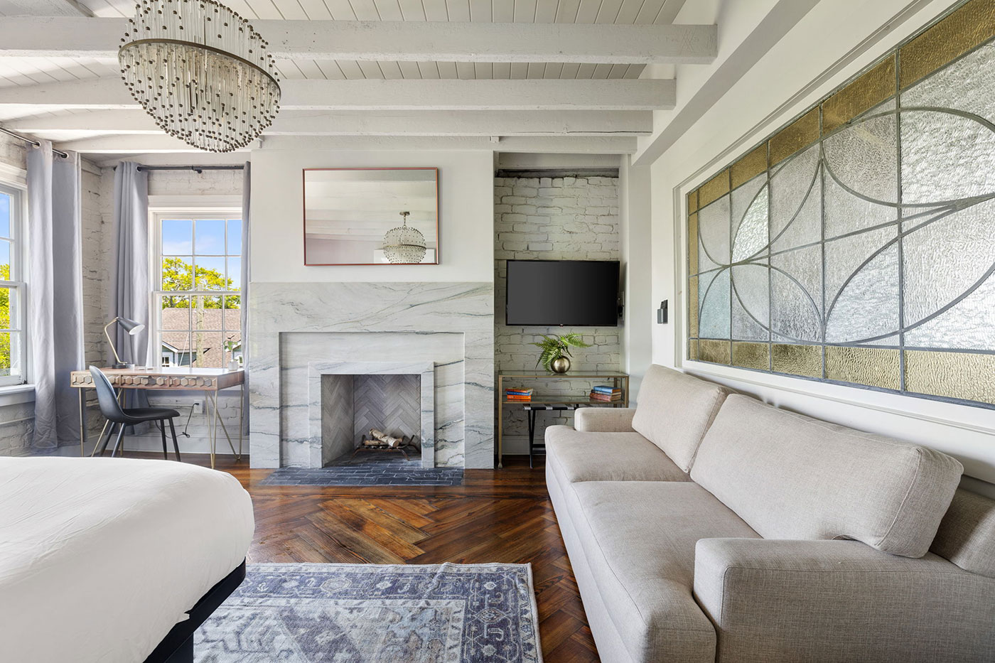 Bright living room with a marble fireplace, flat-screen TV, and gray sofa facing a stained glass window.