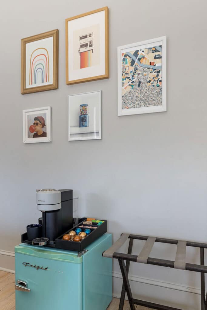 Teal retro mini-fridge converted into a coffee bar with an espresso machine and cups on top, next to a bench.