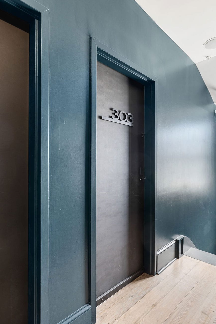 Metal door with the number 303 mounted on a dark surface, set into a blue-green hallway wall.