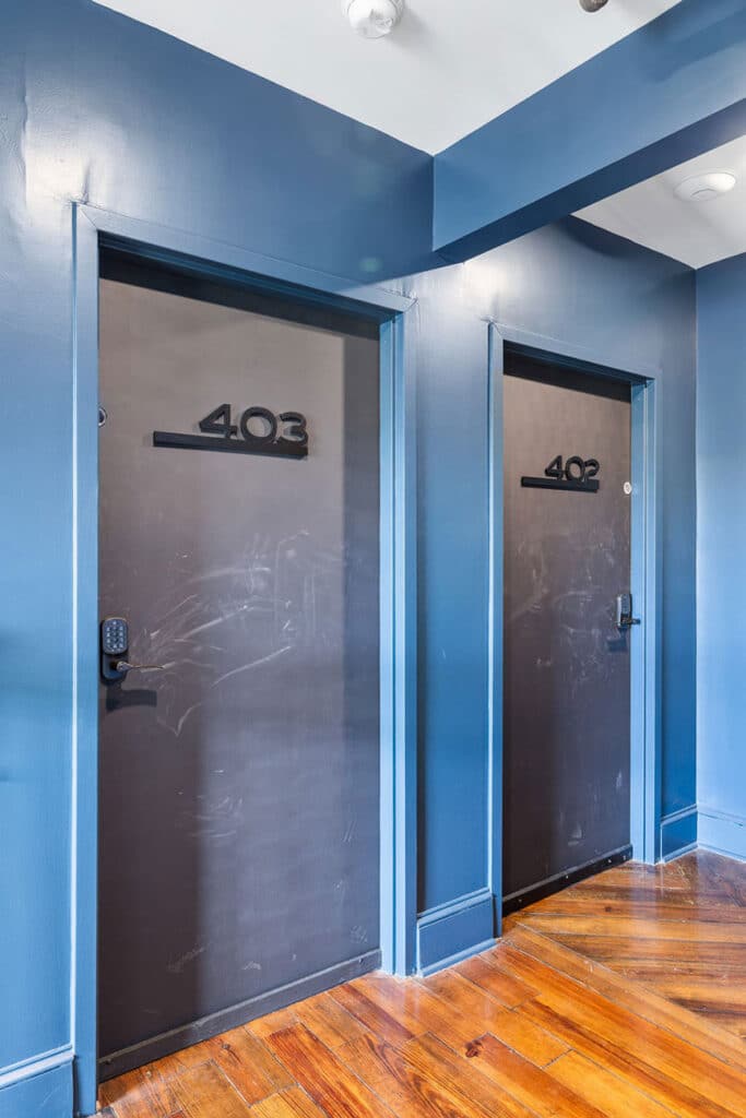 Two dark metal doors labeled 403 and 402 in a blue hallway with a wood floor.