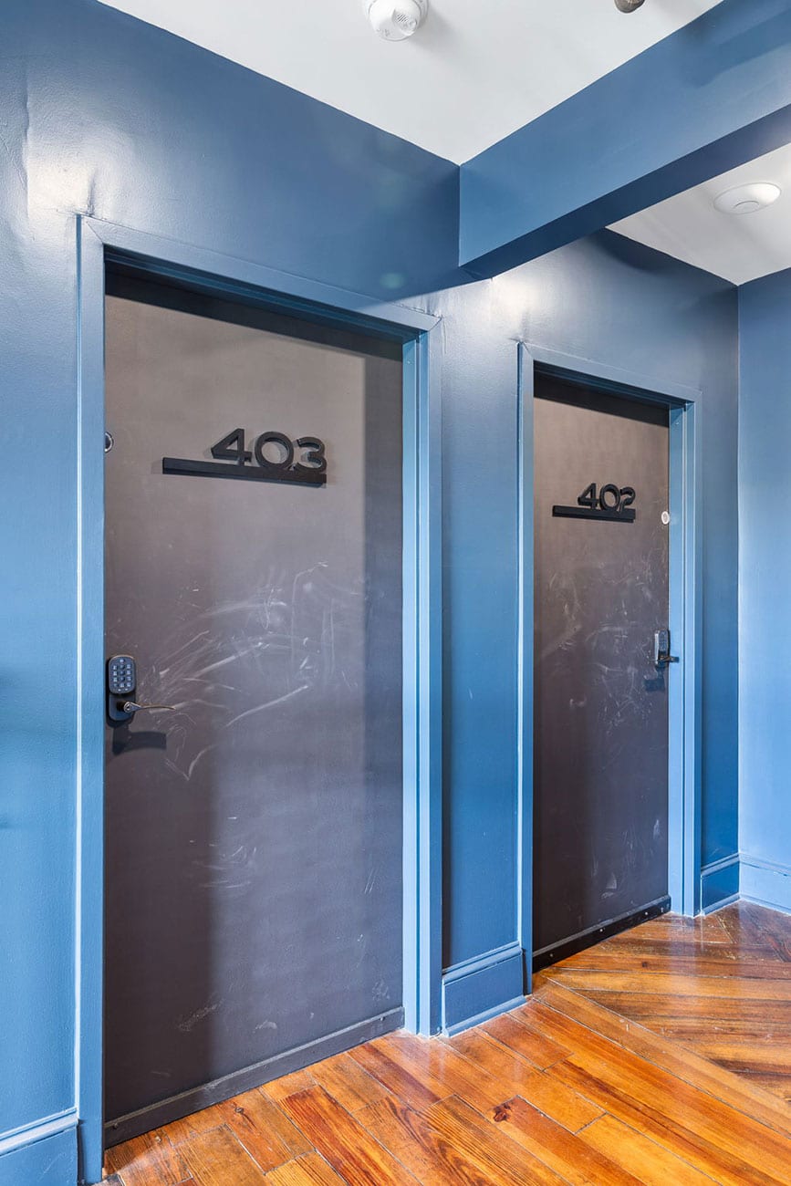 Two dark metal doors labeled 403 and 402 in a blue hallway with a wood floor.