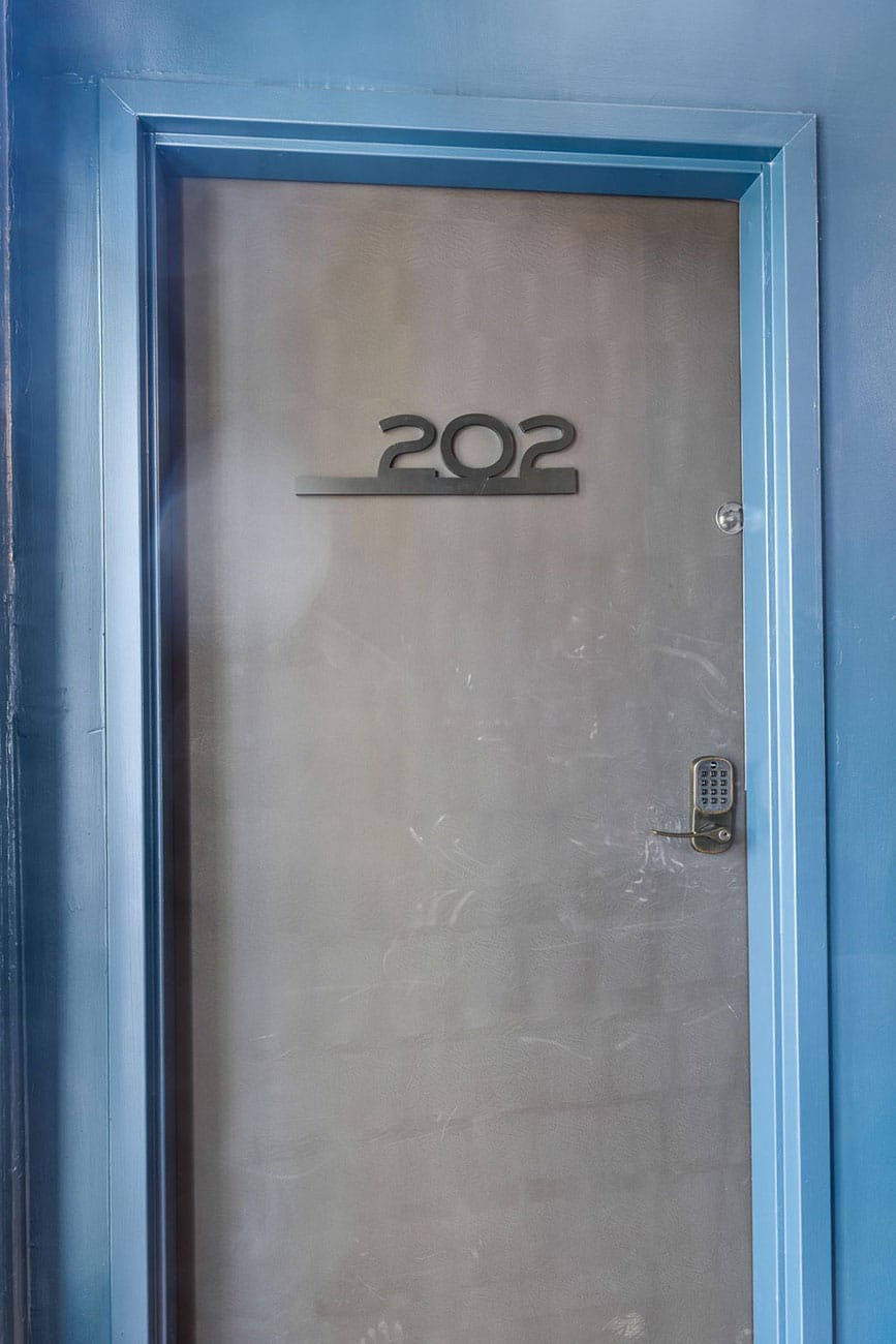 Metal door with blue frame, displaying the number 202 and a keypad lock on the right side.