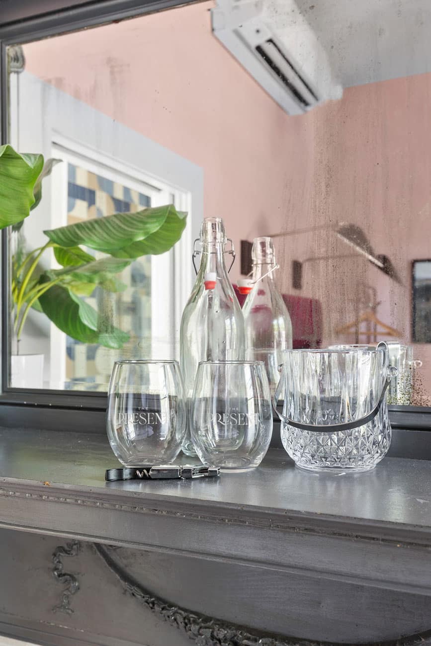 Glass bottles with swing-top caps and several clear tumblers arranged on a windowsill, with a plant in the background.