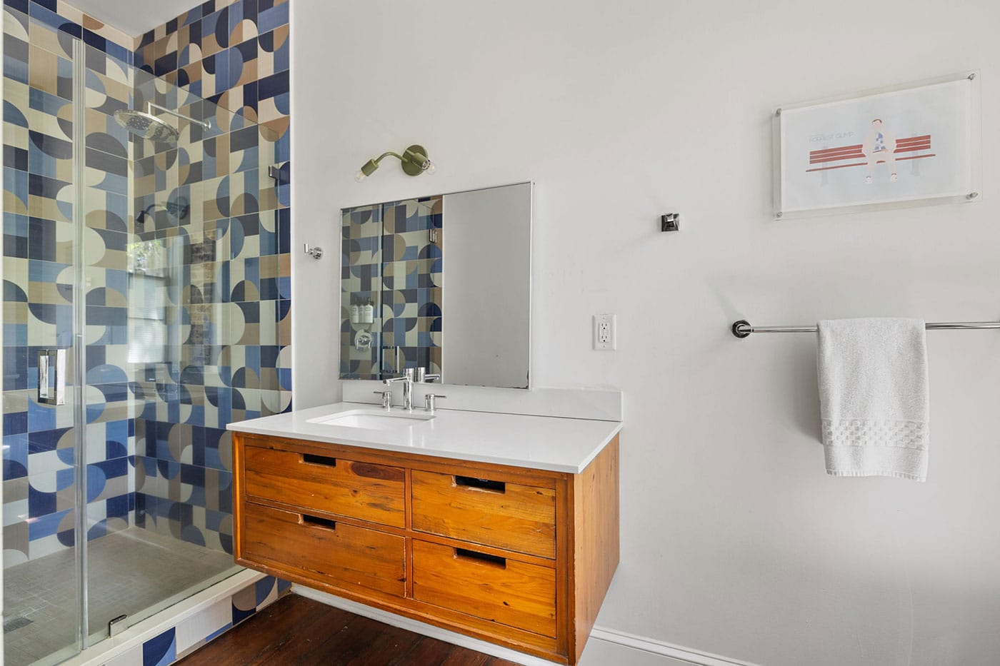 Bathroom with glass-enclosed shower featuring geometric blue tile, plus a wooden vanity with white countertop and sink.