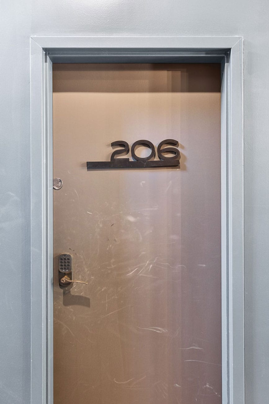 Metal door labeled 206 with a keypad lock on the left side, framed by a light blue wall.