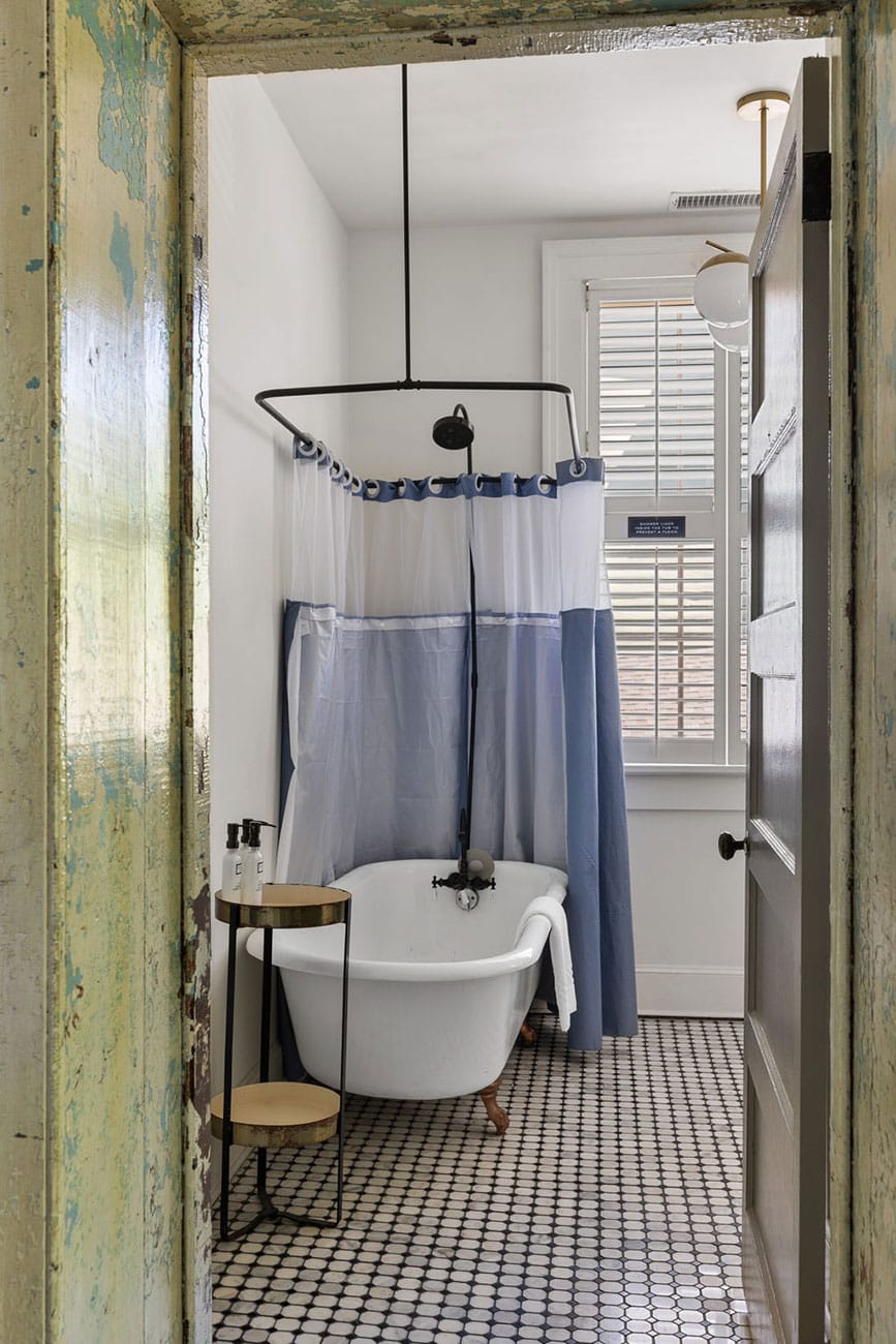 Vintage-style bathroom with a freestanding clawfoot tub, blue-and-white shower curtain, and a small round side table holding dispensers on the tiled floor.