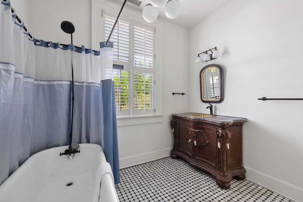 Bright bathroom with a white claw-foot tub, blue-and-white shower curtain, and a dark wooden antique vanity under an oval mirror.